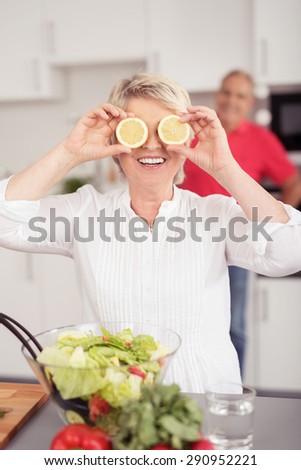 Funny Middle Aged Wife Holding Two Lemon Slices In Front of Eyes While Preparing Fresh Vegetable Salad at the Kitchen.