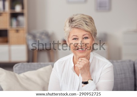 Portrait of a Middle Aged Woman Sitting at the Couch, Leaning her Chin on her Hand While Smiling at the Camera.