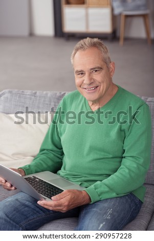 Portrait of a Middle Aged Man Holding his Laptop Computer on His Lap, Sitting on the Couch While Smiling at the Camera.