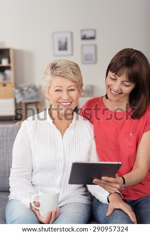 Close up Happy Mom and Daughter with Cup of Coffee and Tablet Computer, Sitting on the Couch at the Living Room.