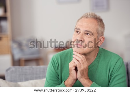 Thoughtful middle-aged man staring into space with a serious expression and his chin resting on his hands, close up view in his living room