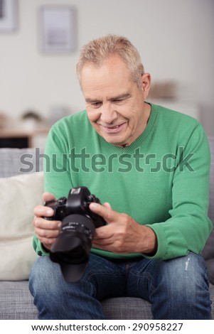 Middle Aged Man in Casual Clothing, Looking at Captured Pictures on DSLR Camera While Sitting at the Couch in the Living Room.
