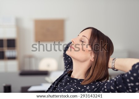 Businesswoman taking time out at work relaxing in her chair at the office with her head tilted back on her clasped hands and eyes closed
