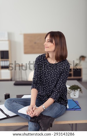 Smiling Thoughtful Office Woman Sitting on a Boardroom Table with Cross Legs, Looking into Distance.