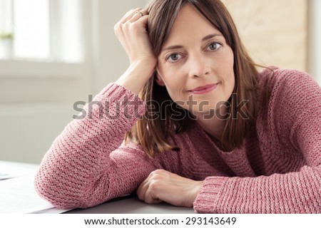 Close up Office Woman in Long Sleeved Shirt, Sitting at her Desk, Leaning on her Arms While Looking at the Camera.