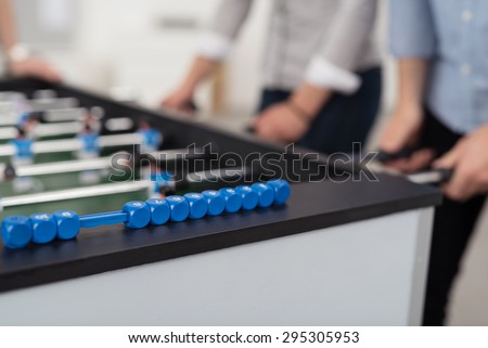 Mid section of two people wearing shirts with rolled up sleeves playing foosball, focus on foreground