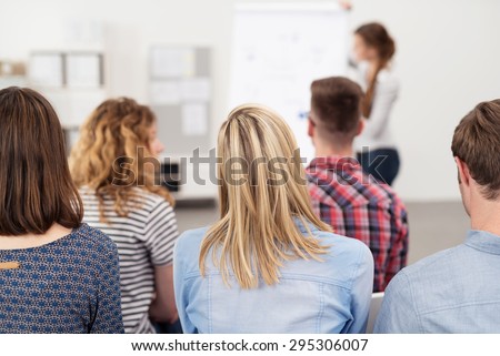 Rear View of Young Office Employees in a Business Meeting Inside the Office, Listening to Someone Presenting Something.