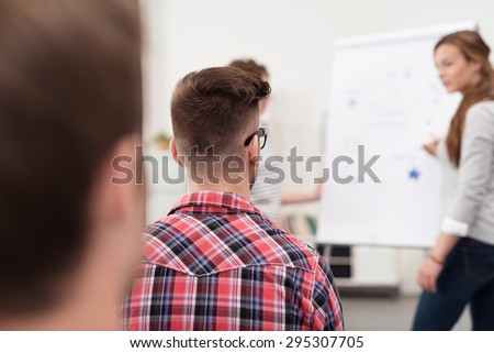 Rear View of a Serious Young Guy Listening to Someone While Presenting Something Using an Illustration.