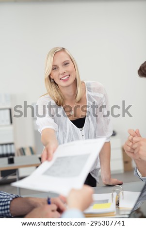 Pretty Young Office Woman Smiling at the Camera While Handing Over a Document to her Co-Worker at the Boardroom Table.