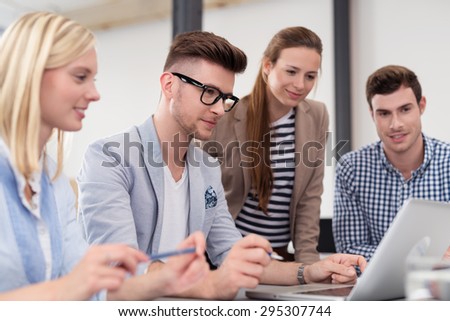 Four Young Office Professionals Watching Something on Laptop Computer on Top of the Table Together