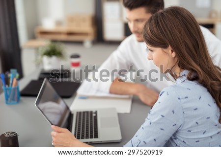 Young Office Woman Watching Something on her Laptop Computer Seriously with her Male Co-worker at her Desk.