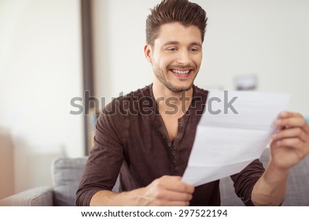 Close up Good Looking Young Bearded Guy Reading a Letter at the Couch with a Happy Facial Expression