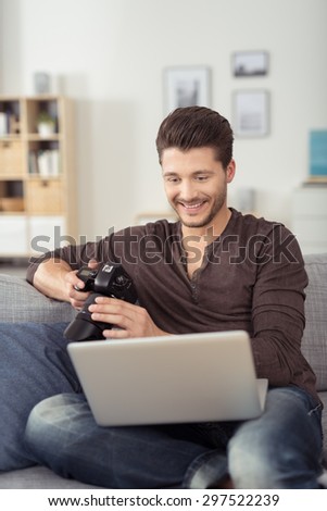 Handsome Young Bearded Man with Laptop Computer and DSLR Camera Relaxing at the Couch with Happy Facial Expression.