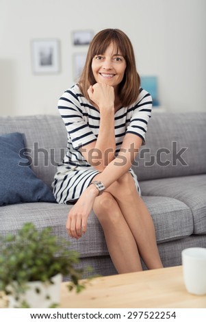 Portrait of a Happy Woman Sitting on the Couch with Legs Crossed and Hand on her Chin, Looking at the Camera