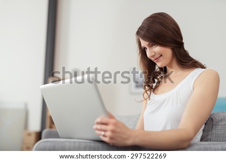 Attractive Young Woman Browsing Internet Using her Laptop Computer at the Couch Inside the House.