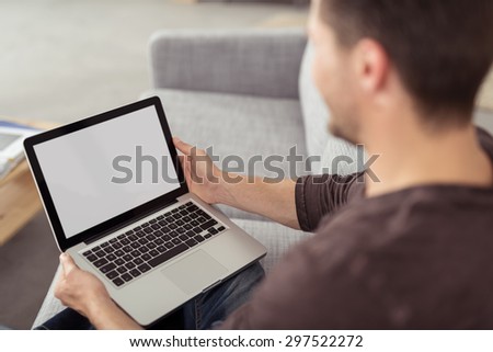 Close up Young Guy Holding his Laptop Computer with Empty Black Screen, Emphasizing Copy Space, While Sitting at the Sofa