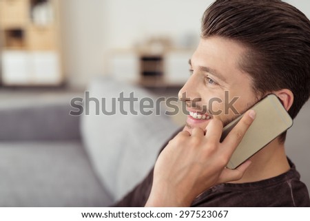 Close up Smiling Attractive Young Guy Talking to Someone Using Mobile Phone While Sitting on the Couch and Looking Into Distance.