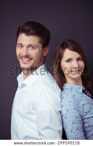 Close up Happy Young Professional Couple in Back to Back Smiling at the Camera Against Gray Wall Background.