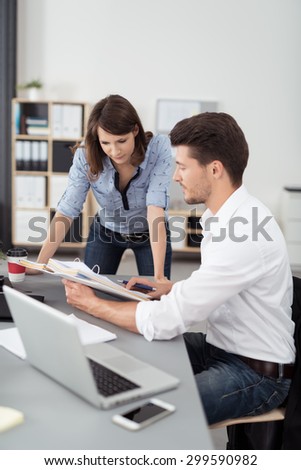 Business couple working on a project together in the office leaning over a desk discussing paperwork in a file, man and woman