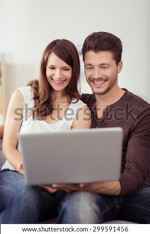 Sweet Happy Young Couple Sitting at the Couch in the Living Room, Watching a Funny Video on Laptop Computer Together.