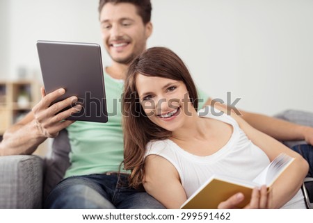 Sweet Young Couple Holding Book and Tablet Computer, Relaxing on the Couch at the Living Room.