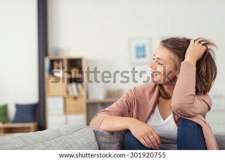Thoughtful Young Woman Sitting on a Couch at the Living Room and Holding Back her Hair While Smiling Into the Distance.