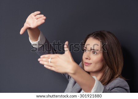 Close up Pretty Young Businesswoman Making Framing Hands Gesture While Looking Into the Distance Against Dark Gray Wall Background.