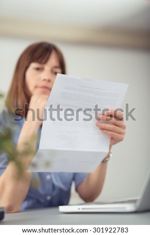 Serious businesswoman sitting at her desk in the office reading a letter or document she is holding in her hand