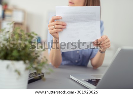 Businesswoman sitting thinking with a folded document in her hands looking off to the side, close up of the sheet of paper and her hand