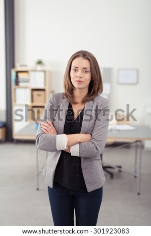 Portrait of a Confident Young Professional Woman Standing Inside the Office with Arms Crossed Over her Stomach and Looking at the Camera.