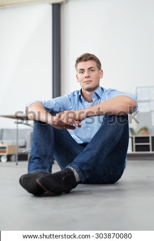 Handsome Young Office Man Sitting on the Floor with Arms Leaning on his Knees and Looking at the Camera