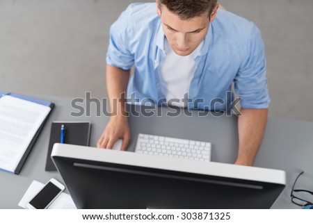 Top View of a Handsome Young Office Guy Sitting at his Workplace and Using his Desktop Computer Seriously
