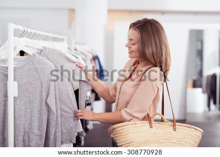 Half Body Shot of a Happy Young Woman with Shoulder Bag Looking at Clothes Hanging on the Rail Inside the Clothing Shop.