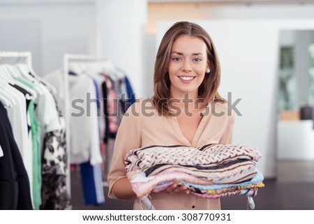 Half Body Shot of a Pretty Young Woman Holding Folded Clothes Inside the Clothing Store.