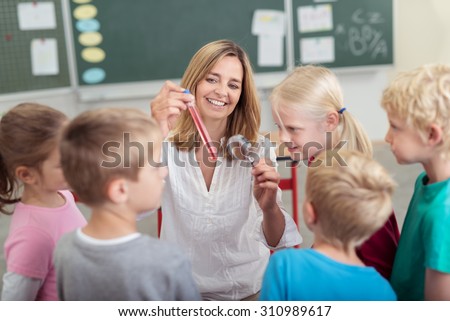 Chemistry teacher showing a chemical solution in a test tube to a group of diverse young schoolchildren in primary school with a happy smile
