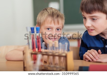 Two young boys doing a chemistry experiment in the classroom at school watching a chemical reaction in test tubes with a smile