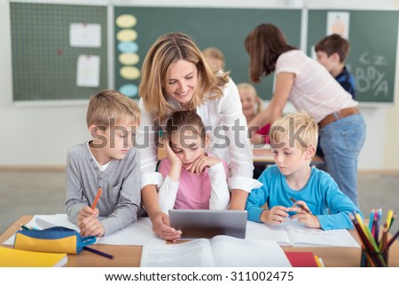 Cheerful Female Teacher with Kids Watching Something Educational Video on Tablet Computer Together Inside the Classroom.