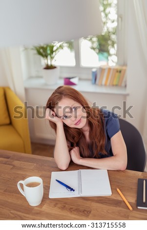 Thoughtful School Girl Leaning on her Elbow on the Wooden Table with Notebook, Pen and a Cup of Coffee While Looking Into the Distance.