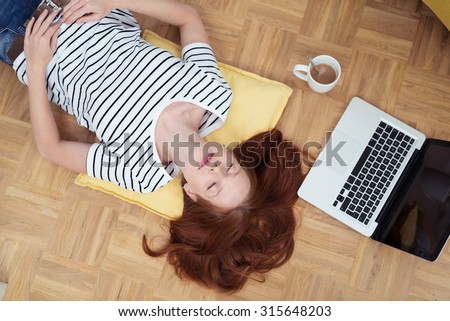 Top View of a Tired Young Woman Taking a Nap on the Floor with a Cup of Coffee and Laptop Computer on her Side.