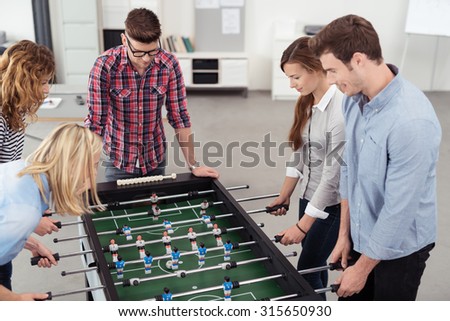Five Young Workmates Enjoying Table Soccer Game Inside the Office During their Break Time.