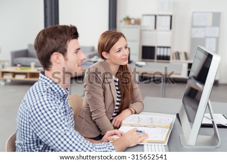 Two Young Office People Looking at the Computer Screen Together On Top of the Desk.