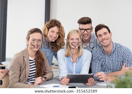 Five Young Office Workers in Casual Clothing, Sitting Inside the Boardroom, Smiling at the Camera.