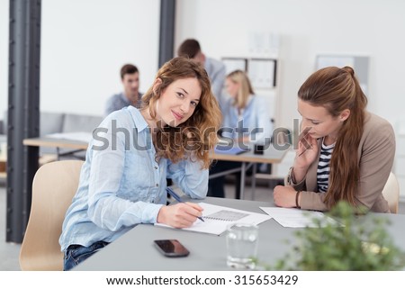 Young Pretty Office Worker Looking at the Camera While in a One-on-One Meeting with her Colleague Inside the Office.