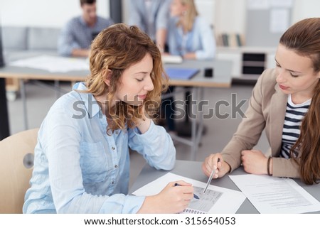 Two Young Attractive Office Women Discussing the Content of a Document on Top of the Table Inside the Office.