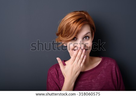 Close up Happy Young Woman Smiling at the Camera While Covering her Mouth with her Hand Against Gray Background with Copy Space.