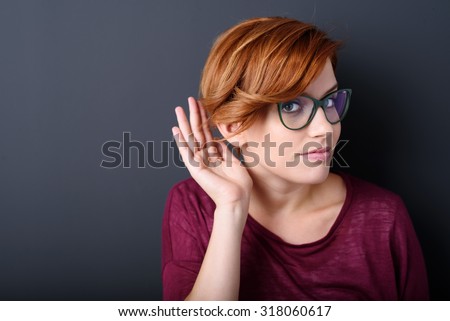 Young woman with a hearing disorder or hearing loss cupping her hand behind her ear with her head turned aside to try and amplify and channel the available sound to her ear drum