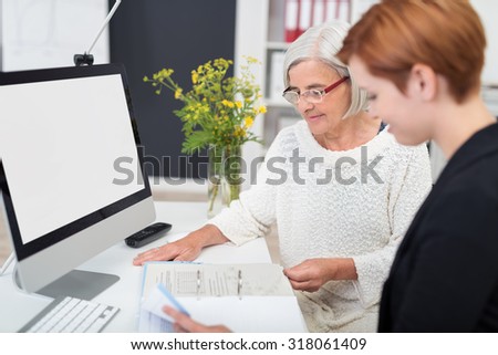 Middle Aged and Young Businesswomen Reading Some Documents at the Table Inside the Office.
