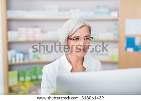 Serious senior female pharmacist working on a computer in the pharmacy checking information on the screen