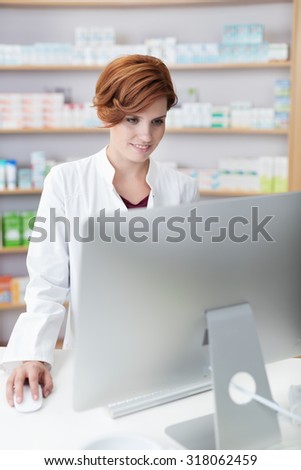Attractive female pharmacist checking information standing reading a large computer monitor on her desk in the pharmacy
