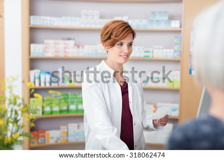 Young pretty redhead female pharmacist assisting on older woman with her prescription medication as she smiles at her over the counter